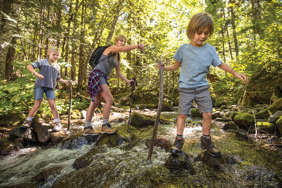 kids hiking boots featured on two people hiking through a stream of water with a woman also wearing hiking shoes